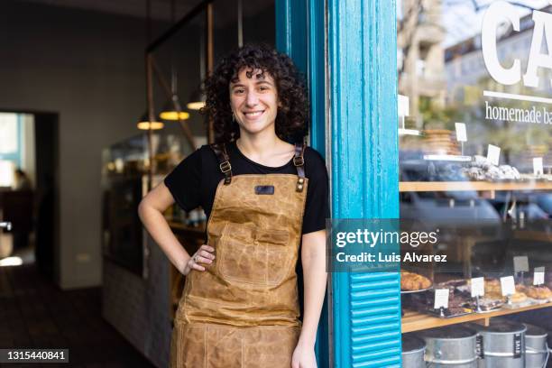 portrait of a non-binary person owner standing in from of their small bakery - mercante foto e immagini stock