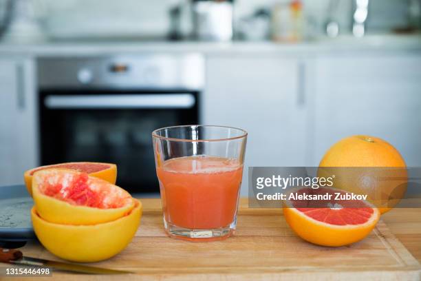 freshly squeezed juice from red ripe grapefruit in a clear glass cup or glass on a cutting board against the background of a wooden kitchen table. i'm making juice for breakfast. the concept of vegetarian, vegan and raw food, detox and diet. - grapefruit red - fotografias e filmes do acervo