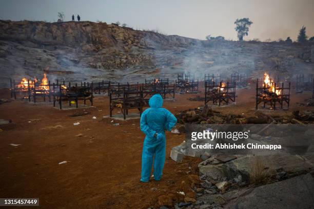 Man wearing PPE watches mass cremations in a disused granite quarry repurposed to cremate the dead due to COVID-19 on April 30, 2021 in Bengaluru,...