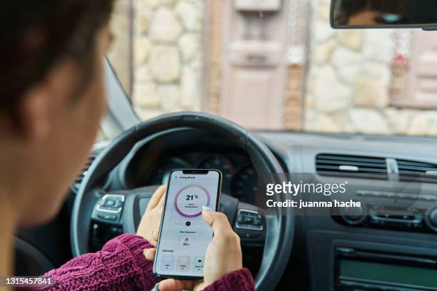 woman controlling the temperature of her smart home from inside her car from a smartphone application - stili foto e immagini stock