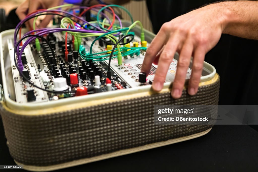 Dj in a live music concert operating a synthesizer in which there are cables of many colors. Concert and music competition