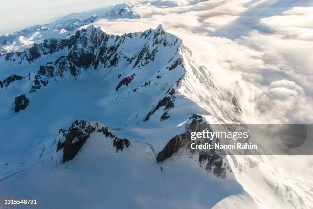 aerial view of snowcapped mountain peak appearing through the clouds - new zealand southern alps stock pictures, royalty-free photos & images