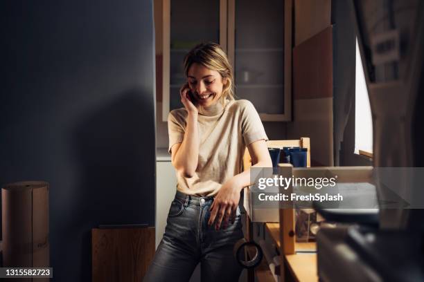 het bewegen uit: gelukkige vrouw die dingen in haar keuken inpakt en op haar mobiele telefoon spreekt - new user stockfoto's en -beelden