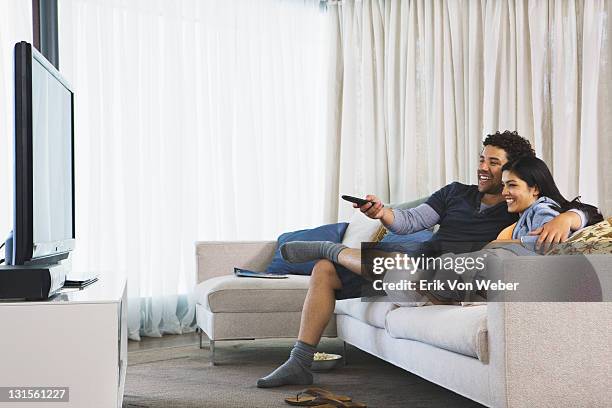 couple watching tv in their home - young people looking at camera foto e immagini stock