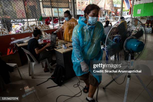 Community volunteer wearing a plastic poncho from Khlong Toei slum cools herself with electric fan inside a village hall converted as a temporary...