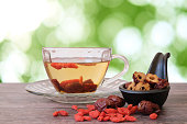 Healthy hot drink brewed from Chinese jujube and Chinese goji berries in glass and sliced dried jujube in the black cup on wooden background with  green blurred garden background.