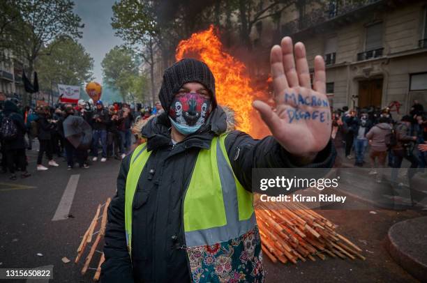 Gilet Jaune, or yellow vest, protestor stands in front of a burning barricade holding his hand up with an inscription calling for President Macron to...