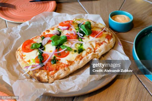 pizza margarita with mozzarella and basil leaves and pesto sauce, on parchment paper, on the table in a cafe or fast food restaurant. traditional italian cuisine. vegetarian food. - tomatenpasta stockfoto's en -beelden