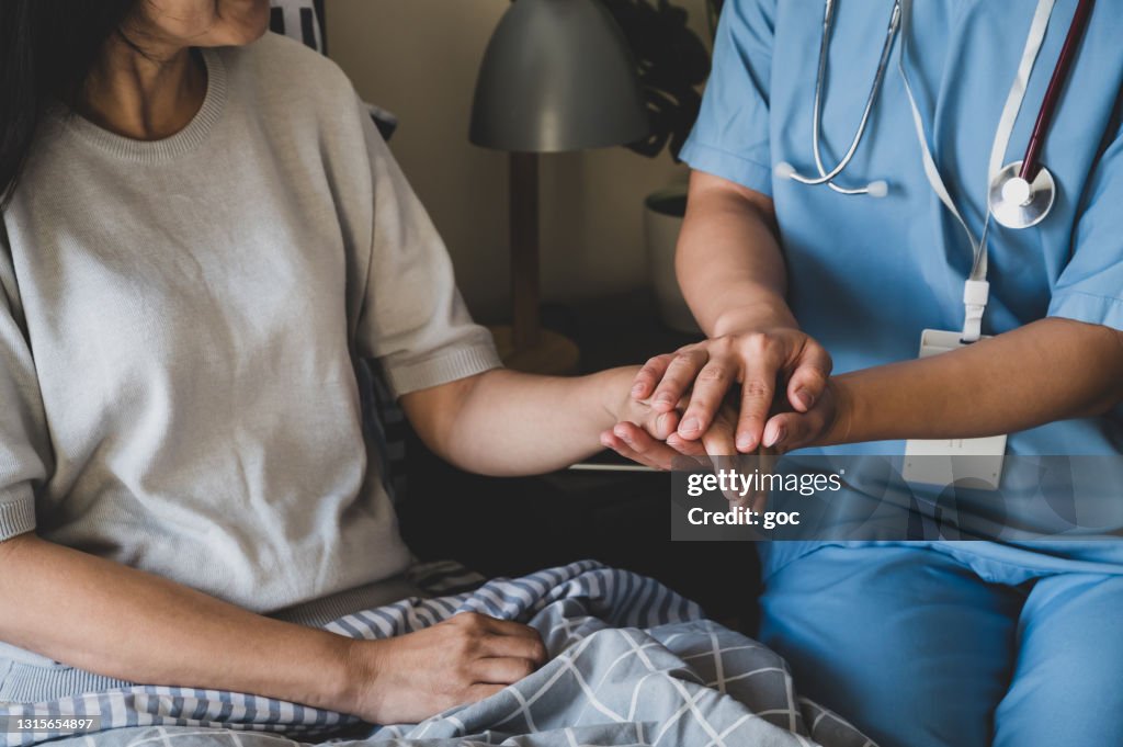 Nahaufnahme einer Krankenschwester, die die Hände hält, um ihre Patientin im Bett zu beruhigen.