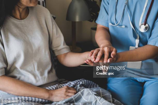 primo posto di un'infermiera che si tiene per mano per rassicurare la sua paziente sul letto. - ethical treatment foto e immagini stock