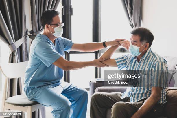 physiotherapist medical specialist giving advice and consulting with senior patient on his shoulder problem, elbow muscle pain problem, physiotherapy exercise and injury rehabilitation in living room during a house visit. - physiology stock pictures, royalty-free photos & images