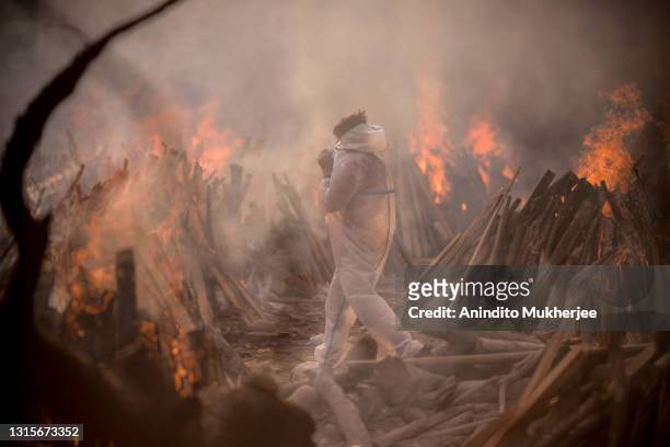 Worker wearing a PPE suit is seen amid the burning funeral pyres of patients who died of COVID-19 at a crematorium on May 01, 2021 in New Delhi,...