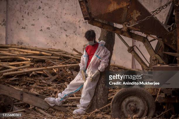 Worker wearing a PPE suit takes a momentary break as people perform the last rites of patients who died of COVID-19 during a mass cremation held at a...