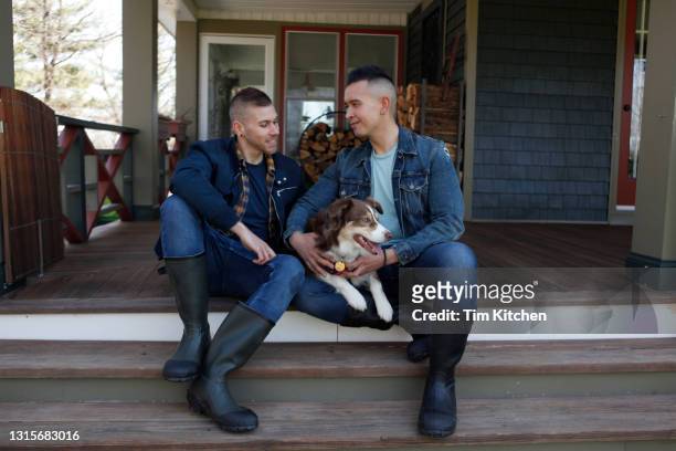 mid-adult male couple sitting on porch with dog - farm couple fotografías e imágenes de stock