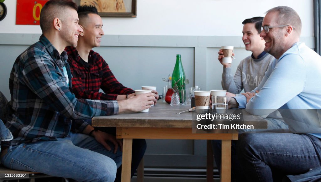 Four mid-adult males looking at each other, smiling and laughing in restaurant