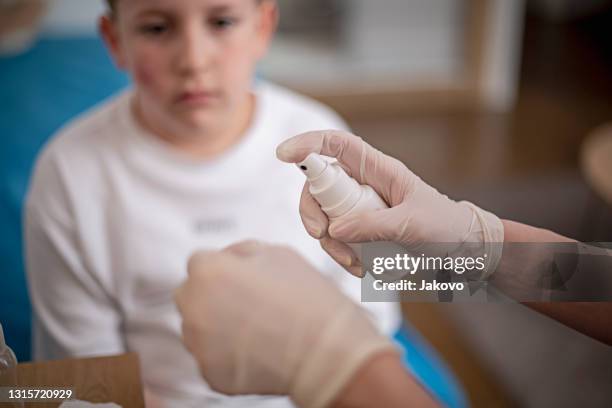 moeder die de wond van haar zoon op zijn wang schoonmaakt - medische procedure stockfoto's en -beelden