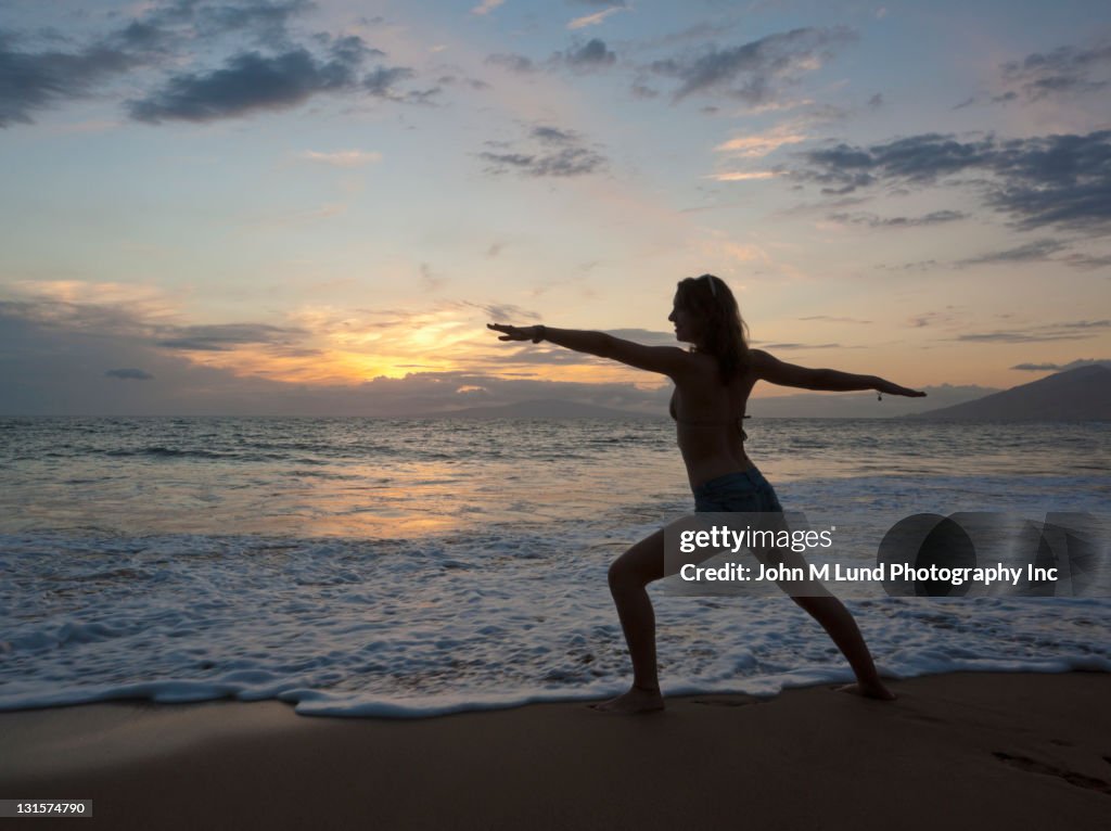 Mixed race woman practicing yoga on beach