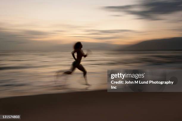 caucasian woman running on beach at sunrise - blurred running sunset stock-fotos und bilder