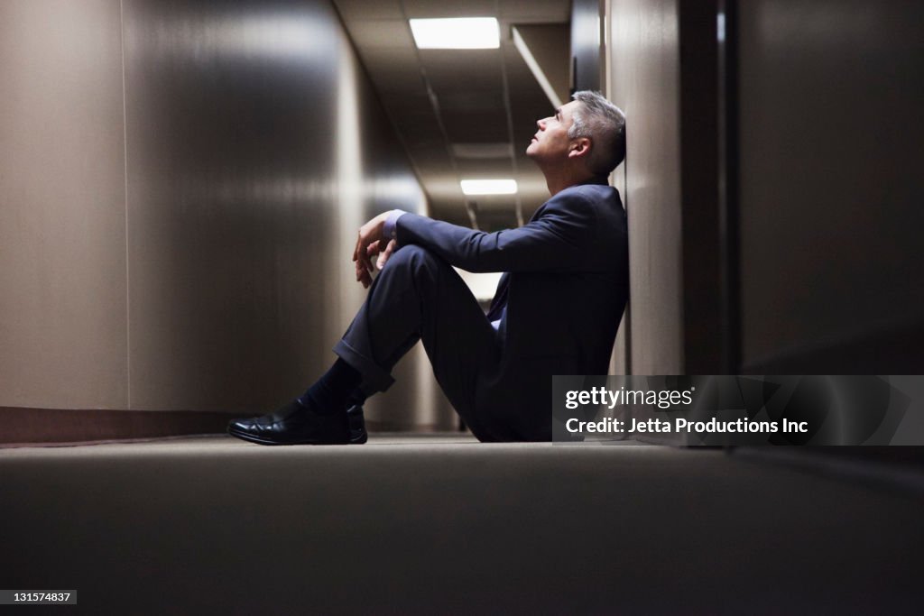 Caucasian businessman sitting on floor in corridor