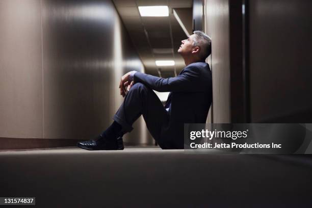 caucasian businessman sitting on floor in corridor - business adversity stock pictures, royalty-free photos & images