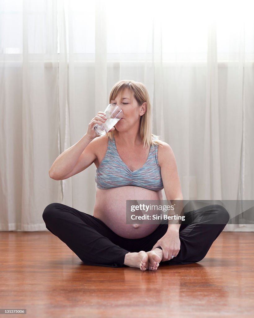 Pregnant Caucasian woman sitting on floor drinking water