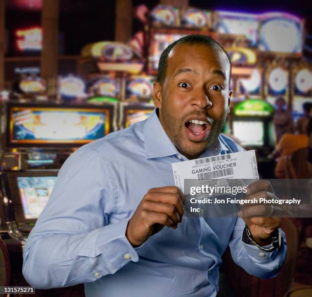 excited african american man holding gaming voucher in casino - winning ticket stock pictures, royalty-free photos & images