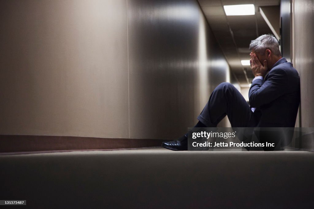 Caucasian businessman sitting on floor in corridor