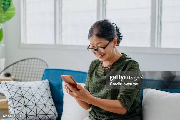 happy senior woman using smartphone at home - asian woman on call stock pictures, royalty-free photos & images