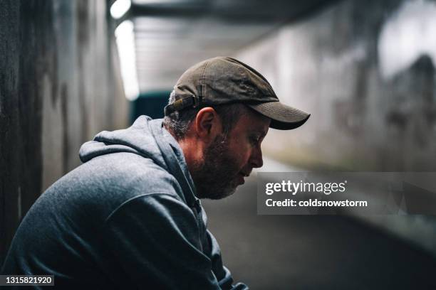 obdachloser depressiver mann in dunklem u-bahn-tunnel - beggar stock-fotos und bilder