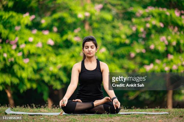 young woman meditating outdoors at park - serene people stock pictures, royalty-free photos & images