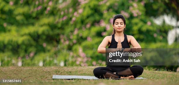 young woman sitting in namaste or prayer yoga position and relaxing at park - yoga stock pictures, royalty-free photos & images