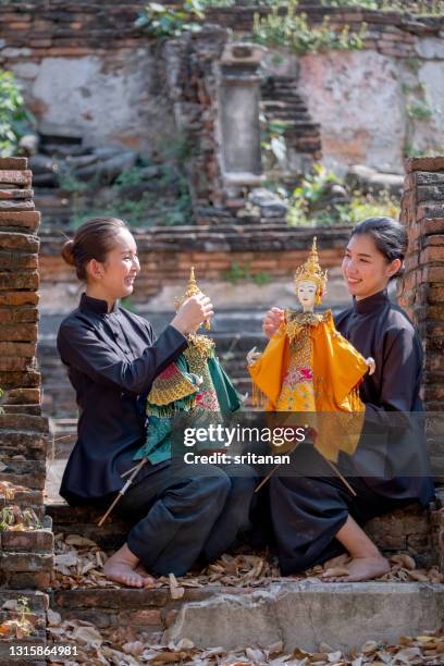 two asian teen girls relax after practice thai puppet show with siting on step or stair of ancient temple building - songkran stock pictures, royalty-free photos & images