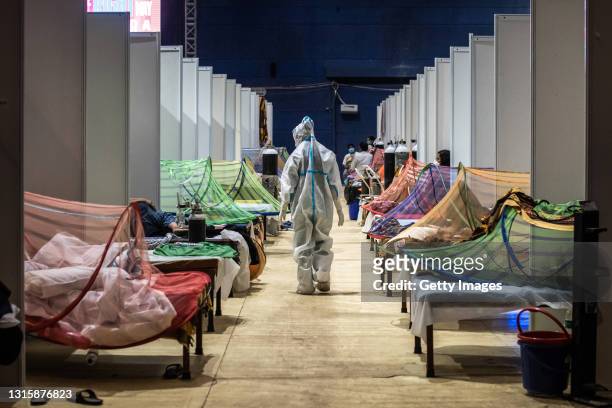Medical worker in PPE observes patients who have been infected by Covid-19 inside a makeshift covid care facility in a sports stadium at the...