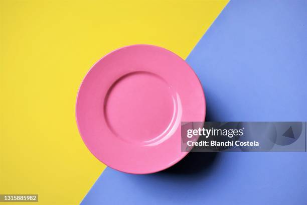 pink plate on blue and yellow background - blue plate stock pictures, royalty-free photos & images