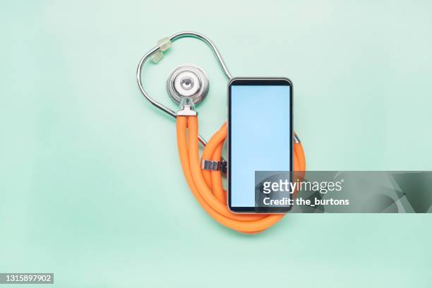 high angle view of stethoscope and mobile phone on turquoise background, telemedicine - doctor using smartphone stock-fotos und bilder