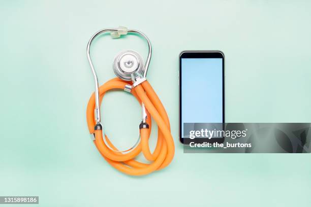 high angle view of stethoscope and mobile phone on turquoise background, telemedicine - stethoskop stock-fotos und bilder