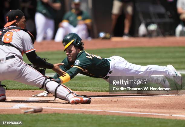 Ramon Laureano of the Oakland Athletics scores sliding under Pedro Severino of the Baltimore Orioles in the first inning at RingCentral Coliseum on...