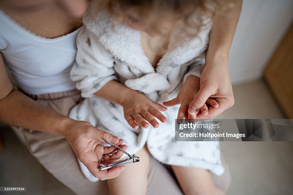 Unrecognizable mother with small daughter in bathroom at home, cutting nails after bath.