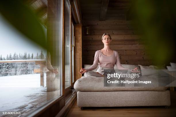 mid adult woman relaxing indoors on winter holiday, doing yoga. - yoga in the snow stock-fotos und bilder