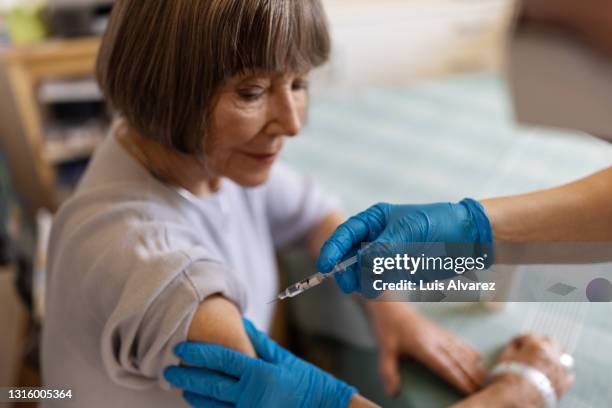 elderly woman getting vaccination on arm at home - injection stock-fotos und bilder