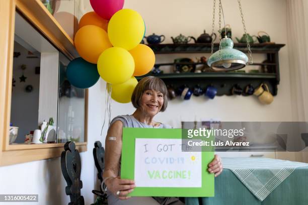 elderly woman with "i got the covid-19 vaccine" sign at home - state of emergency sign stock pictures, royalty-free photos & images