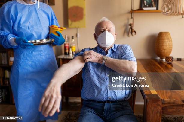 retired man getting ready covid-19 vaccination at home - roll up stockfoto's en -beelden