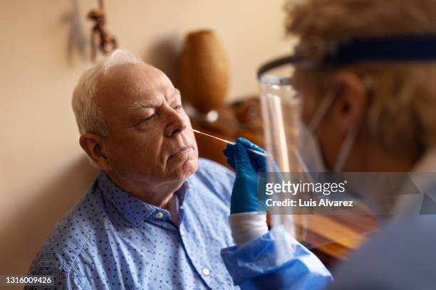 medical worker in ppe performing nasal swab covid-19 test at home - pcr gerät stock-fotos und bilder