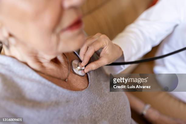 sick senior woman being examined by a doctor - listening to heartbeat stockfoto's en -beelden