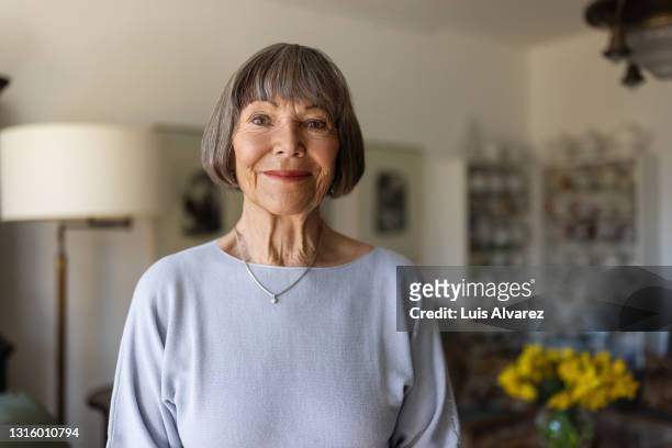 portrait of a happy senior woman standing in her home - femme salon photos et images de collection