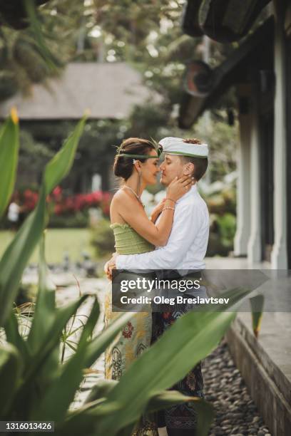 young and happy wedding couple in balinese traditional dress. multicultural destination wedding in bali. - indian honeymoon couples stock pictures, royalty-free photos & images