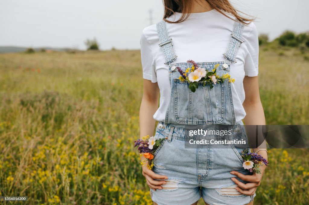 Junge Frau mit Blumen in Taschen zu Fuß auf grünen Frühlingsfeldern