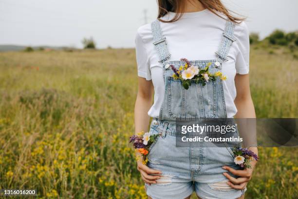 young woman with flowers in pockets walking on green spring fields - jeans pocket stock pictures, royalty-free photos & images