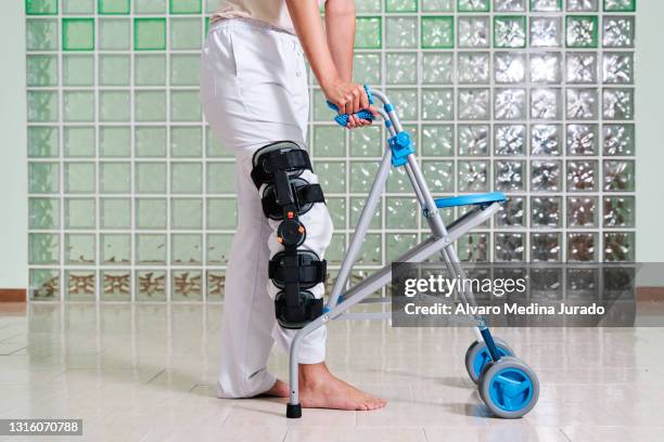 patient walking in a physiotherapy clinic using a walker and a knee brace on his leg to treat a knee injury. - standing with hands on knees imagens e fotografias de stock