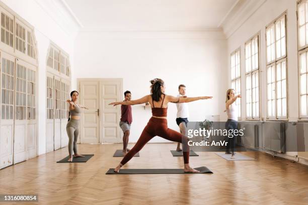group of people in warrior 2 pose in a bright yoga studio - yoga instructor stock pictures, royalty-free photos & images